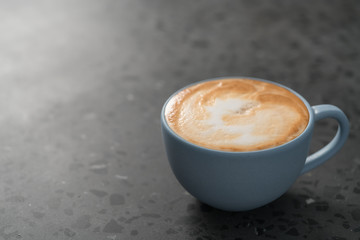 Fresh cappuccino in blue cup on concrete background