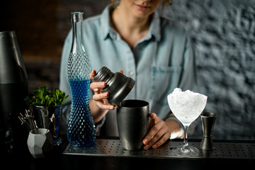 Close-up girl bartender accurate closes shaker lid.