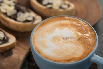 Fresh cappuccino in blue cup with toasts with chocolate spread on concrete background