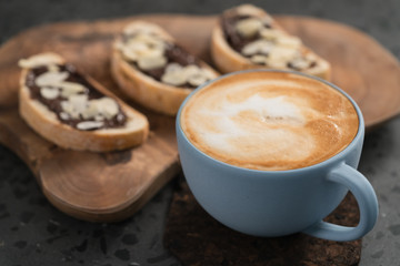 Fresh cappuccino in blue cup with toasts with chocolate spread on concrete background