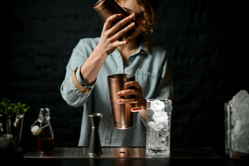 young woman at bar holds in her hands two metal cups.