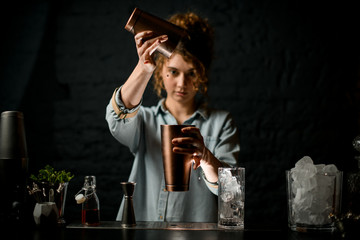 young girl at bar pours drink from one metal cup to another and looks at it.