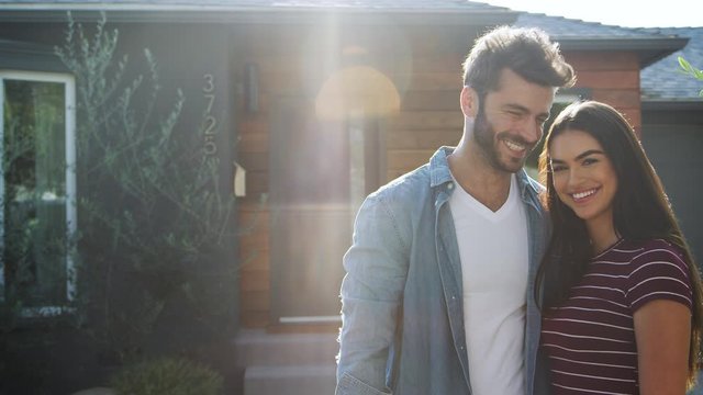Portrait Of Hugging Couple Standing Outdoors In Front Of House Against Flaring Sun
