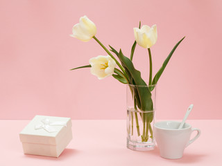 Bouquet of yellow tulips in vase with gift box on a pink background.
