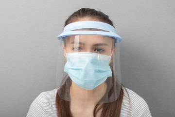 Coronavirus Remedy Young woman in a protective mask screen with a visor on a gray background