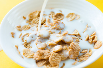 Breakfast ingredients. Cereals with milk. Top view, A bowl of corn flakes and raisins, pouring milk into bowl of corn flakes, top view