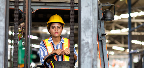 African american Woman forklift worker operator driving vehicle wearing safety goggles and hard hat at warehouse