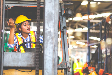 African american Woman forklift worker operator driving vehicle wearing safety goggles and hard hat...