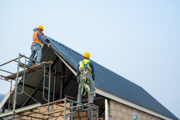 Roofer using air or pneumatic nail gun and installing metal roof tile on top roof,Builder Working...