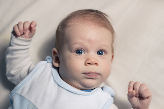 Cute, happy, long hair, blue eye, salivating baby lying on sheet.