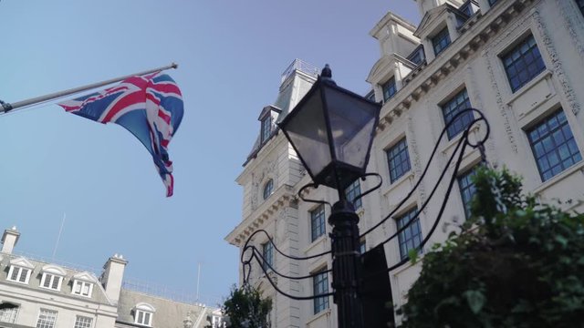 British flag is flapping near to a traditional street lamp on a clear blue sky around Victorian architecture buildings