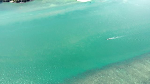 Aerial of small boat in hot tropical green waters by summer islands with coral reef