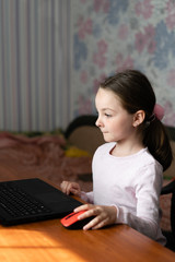 Fototapeta na wymiar little ethnic girl sitting at home at the table and working on homework on a laptop,