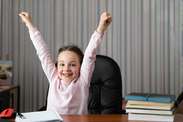 Beautiful little at the desk. Fun rejoices life raises his hands up.