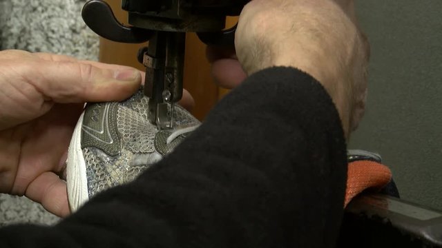 Cobbler sewing torn sport shoe on old sewing machine, closeup