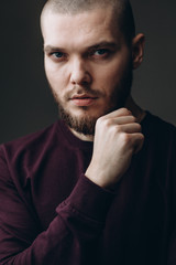 Serious young man looking in a frame on a gray background. bald with a beard