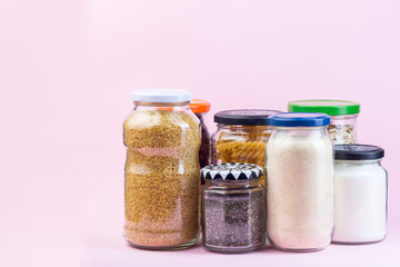 Different food in reused glass jars on a pink background, zero waste plastic free concept, horizontal, copy space