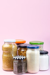 Different food in reused glass jars on a pink background, zero waste plastic free concept, vertical, copy space