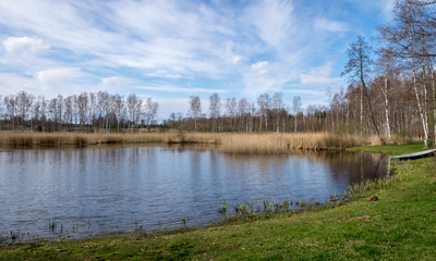 Fototapeta na wymiar sunny spring day landscape, bright blue sky with white clouds, reflected in the lake water