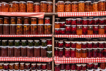 Glass jars with various types of natural delicious jam stand in a row on wooden shelves