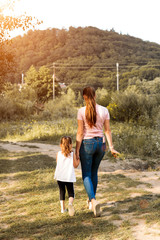 Fototapeta premium Beautiful couple child girl with mother are walking in spring garden with pink blossom roses flowers, sunset time