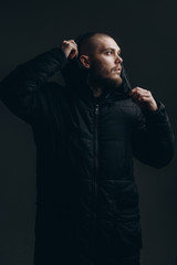 close-up portrait of a serious young man in a jacket looking to the side on a gray background. bald with a beard