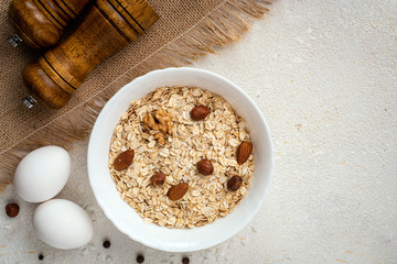 Fototapeta na wymiar Dry oatmeal with nuts and eggs in a white plate on a white background. Healthy breakfast concept. Top view, copy space.