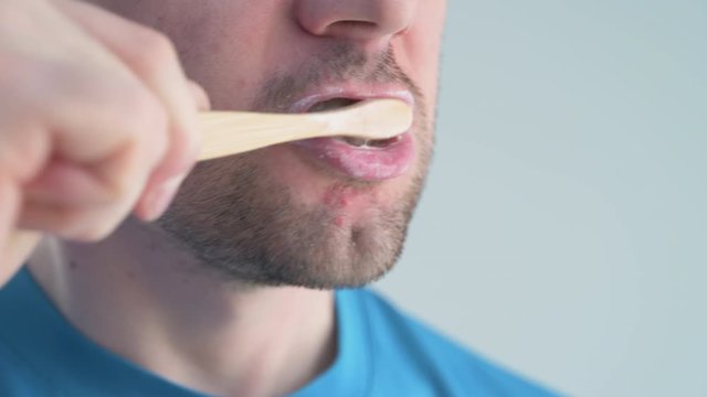 Adult Caucasian man brushes his teeth with a bamboo toothbrush in a light bathroom. Without plastic, zero waste. Close-up, copy space.