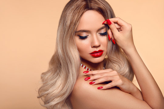 Makeup & manicured nails. Beauty portrait of blonde woman with red lips, long healthy shiny blond hair style. Sensual girl with bright makeup isolated on beige backhround.