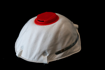 White N95 respirator face mask with red filter isolated on black background, rubber bands tucked...