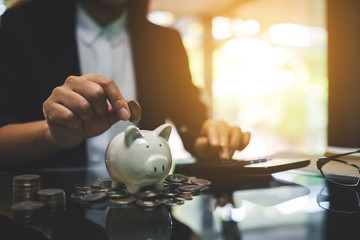 Businesswoman calculating and putting coin into piggy bank for saving money and financial concept