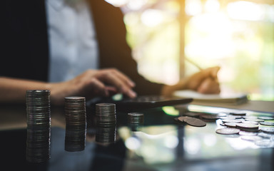 Businesswoman calculating with coins stack on the table for saving money and financial concept