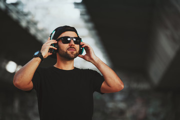 Young man with black hat and sunglasses listening to music via headphones in the city