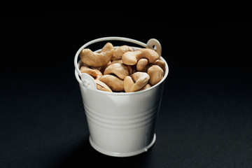 Against a dark background, peeled cashew nuts were poured into a small bucket