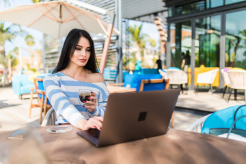 Technology and travel. Working outdoors. Freelance concept. Pretty young woman using laptop in cafe on tropical beach.