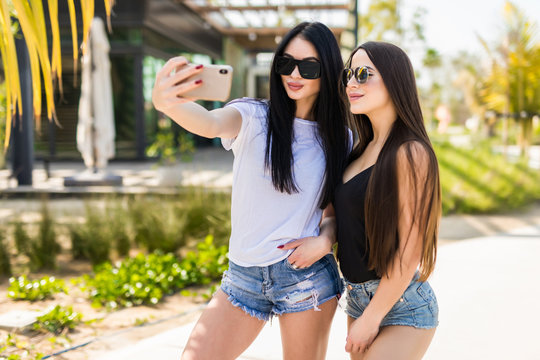 Portrait of funny pretty best friends girls having fun making selfie outdoors in summer