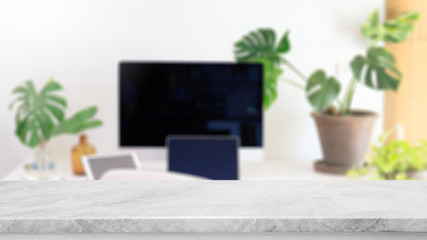 Empty white marble stone table top and blurred home interior with green leaf and computer laptop on table in living room background. - can used for display or montage your products.