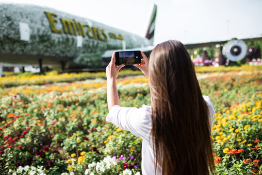 Young pretty woman tourist take photo on the phone with frowers airplane in miracle garden