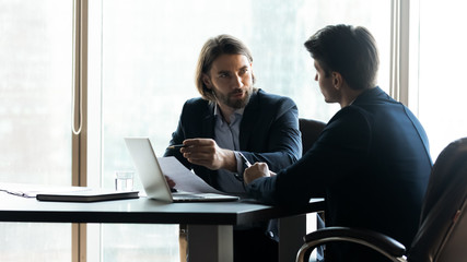 Confident businessman pointing at laptop screen, discussing project strategy with colleague,...