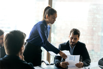 Confident businesswoman mentor giving papers, business strategy documents to employees at corporate...