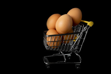 Eggs. Mini supermarket trolley with brown eggs on a black background.