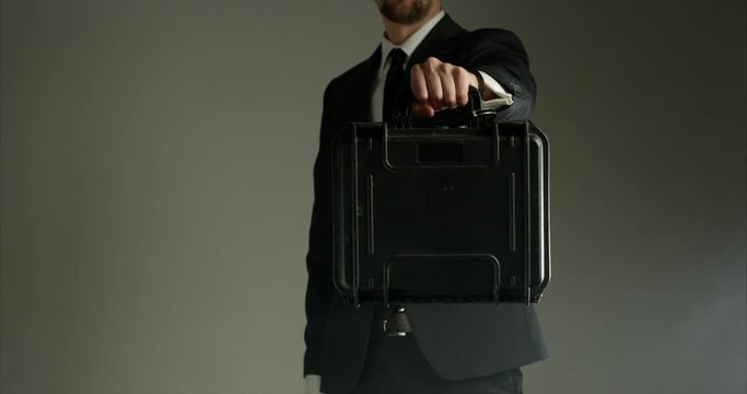 Man in business suit with briefcase handcuffed to wrist - points briefcase towards camera - close up