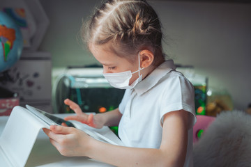 Fototapeta na wymiar Caucasian preteen girl with medical mask on her face concentrated on her task with tablet. Concept of distance learning in isolation while coronavirus.