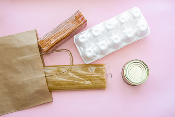 Paper bag with grocery food on a red background. Food delivery home during quarantine: noodles, canned food, buckwheat, crackers.
