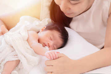 Fototapeta na wymiar Selective focus beautiful Asian mother with wedding ring nurturing adorable infant with love and care, mom hold tiny finger newborn baby while sleeping comfortable on bed at home. motherhood lifestyle