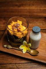 A cup of mango sticky rice on a wooden table. Thai dessert with coconut milk