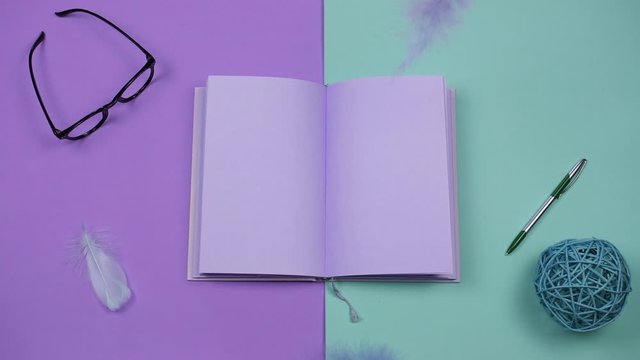 Creative, art and wright concept. Pastel violet book isolated on a two colored background, colored feathers falling on a notebook with empty pages