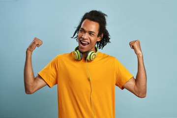 Fototapeta premium Joyed black man raises clenched fists, feels energized and upbeat, on blue wall