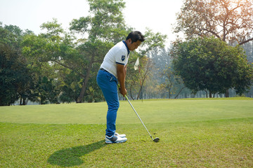 Golf player hitting shot with club on course at beautiful morning with sun flare in background