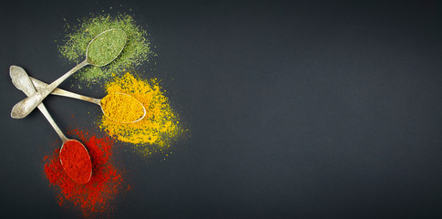 Types of various spices in spoons on a dark table. Spices for food. Food background. Banner. Copy space.